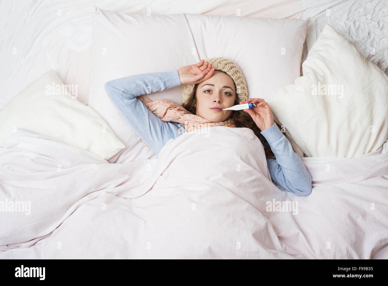 Malata con il termometro è giacente in letto. Ella ha freddo, influenza e febbre alta. Foto Stock