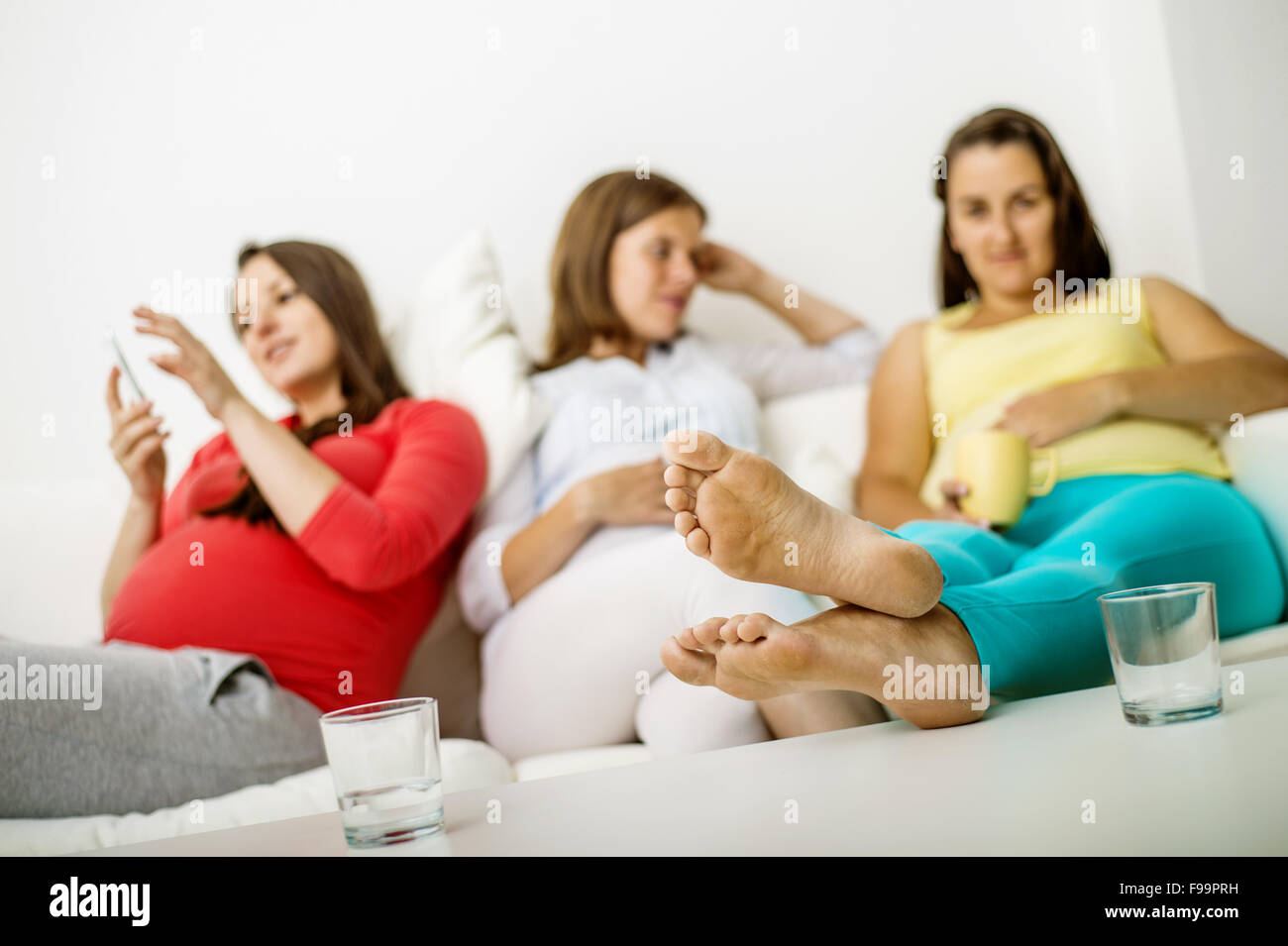 Tre donne in stato di gravidanza seduti sul divano e posa Foto Stock