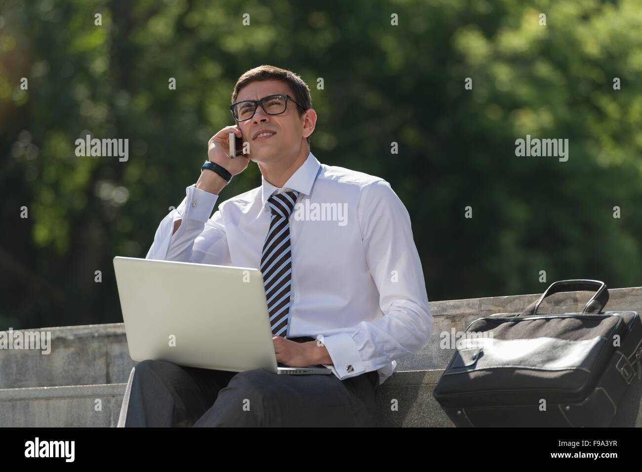 Uomo con notebook chiamando dal telefono al parco estivo sul luminoso giorno Foto Stock