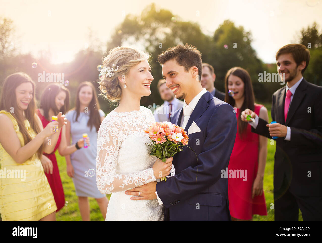 I giovani sposi novelli godendo momento romantico insieme al ricevimento di nozze al di fuori, ospiti di nozze in background a soffiare bolle Foto Stock