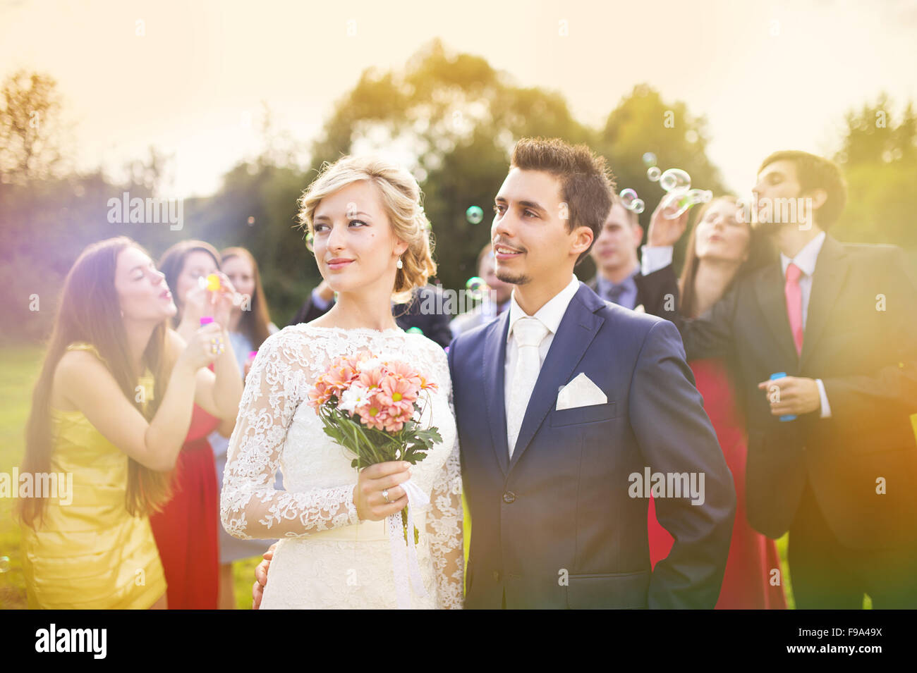 I giovani sposi novelli godendo momento romantico insieme al ricevimento di nozze al di fuori, ospiti di nozze in background a soffiare bolle Foto Stock