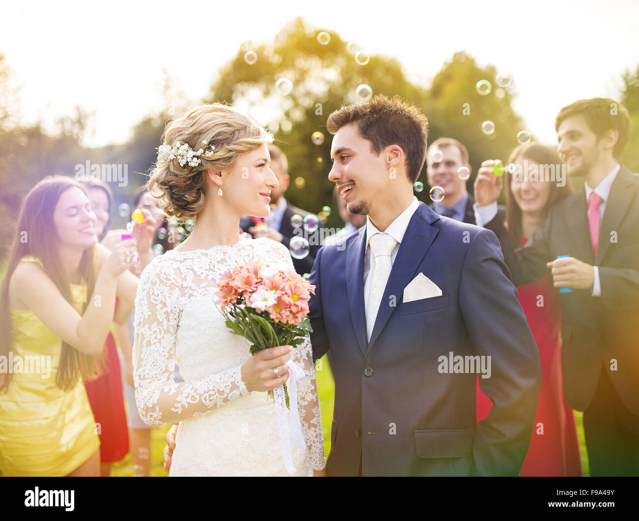 I giovani sposi novelli godendo momento romantico insieme al ricevimento di nozze al di fuori, ospiti di nozze in background a soffiare bolle Foto Stock