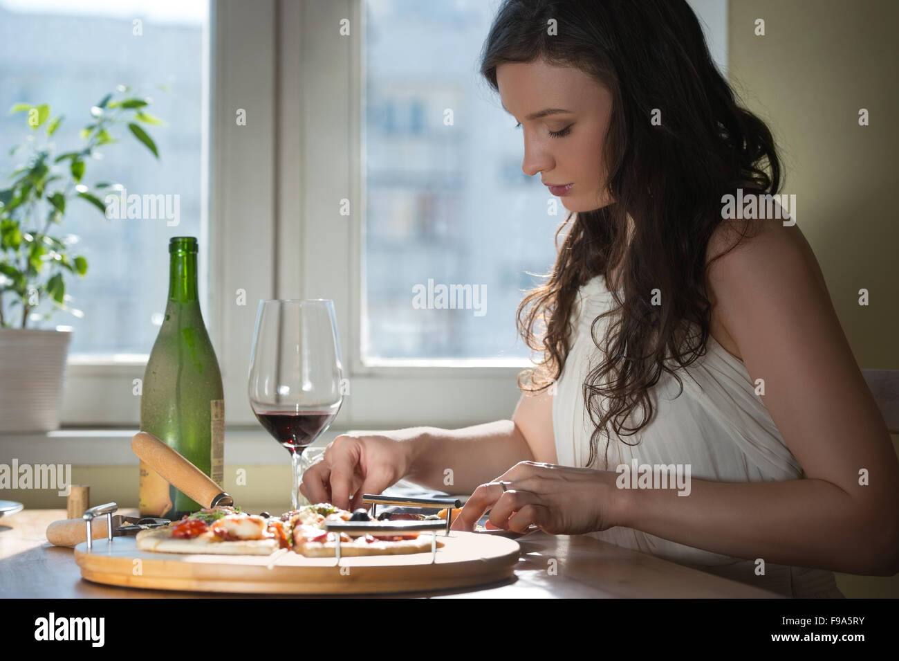 Bella giovane donna di mangiare la pizza fatta in casa e di bere il vino rosso a casa Foto Stock