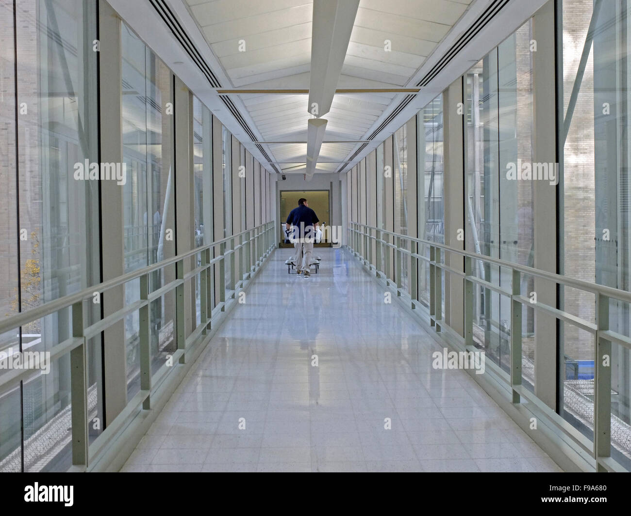 Un ospedale lavoratore spingendo un letto in un cavalcavia presso il monte Sinai san Luca oltre 114Street a Manhattan NYC. Foto Stock