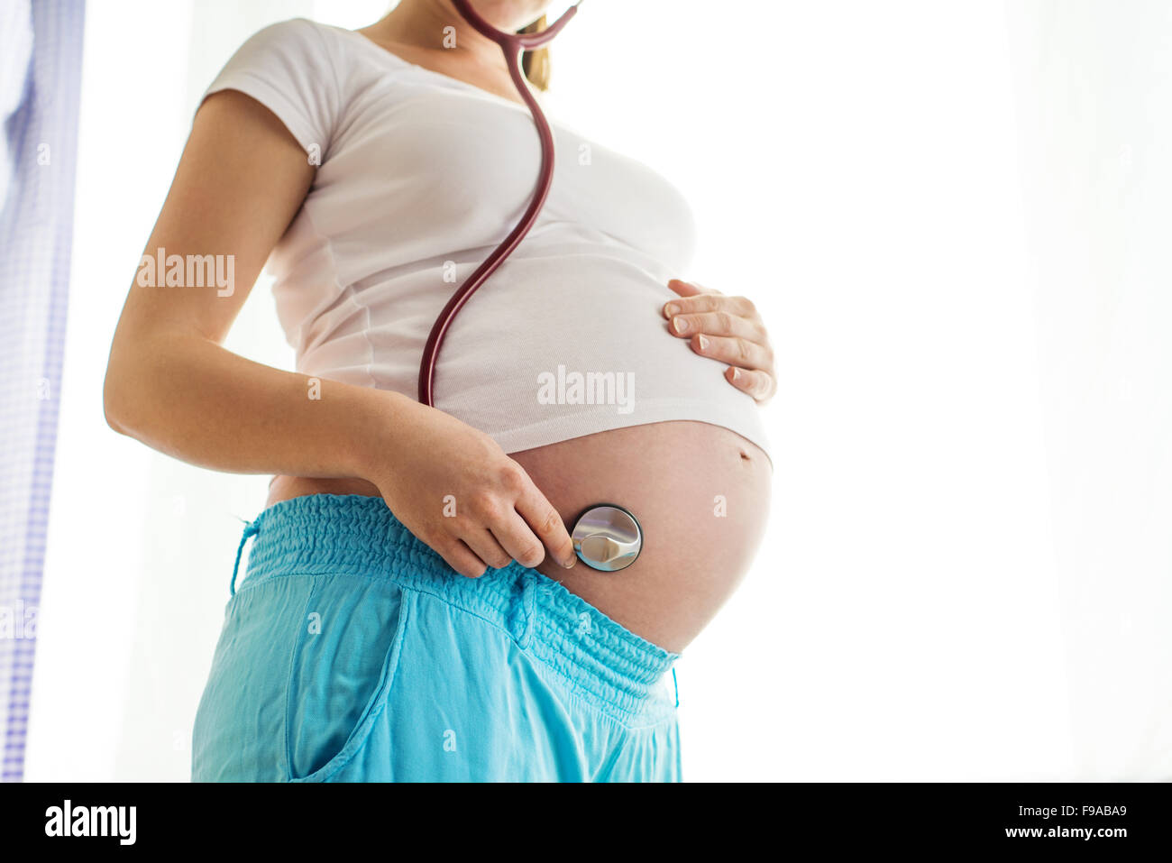 Close-up di un irriconoscibile donna incinta con sthetoscope e le mani sulla pancia Foto Stock