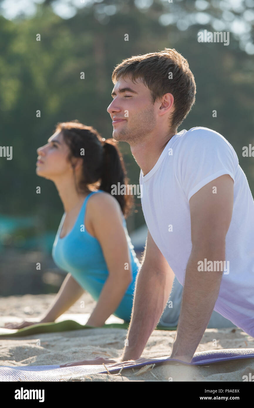 Coppia giovane facendo stretching esercizi yoga con il mare sullo sfondo Foto Stock