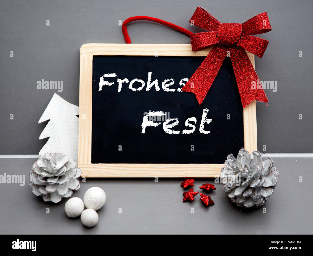 I tedeschi 'Frohes Fest' (Merry Christmas) scritti sulla lavagna con un nastro rosso e pigne Foto Stock