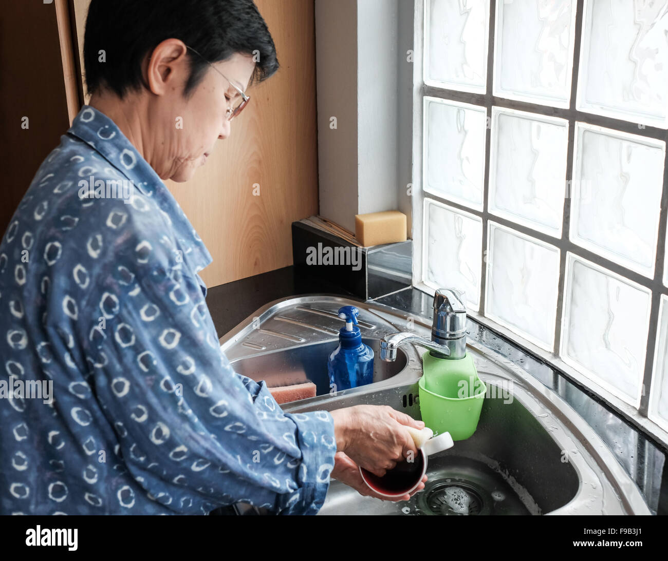 Donna Thai tazze di pulizia presso il lavello della cucina Foto Stock