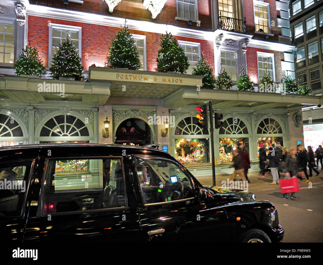 Fortnum & Mason ingresso del negozio durante la notte con la festosa accesa alberi di Natale acquirenti e London Black Cab in primo piano London REGNO UNITO Foto Stock