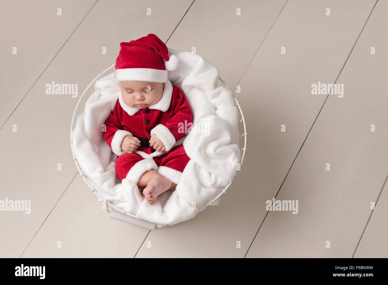 Tre mesi di età bambina indossa un Santa Claus costume e dormire in un cesto in filo. Foto Stock