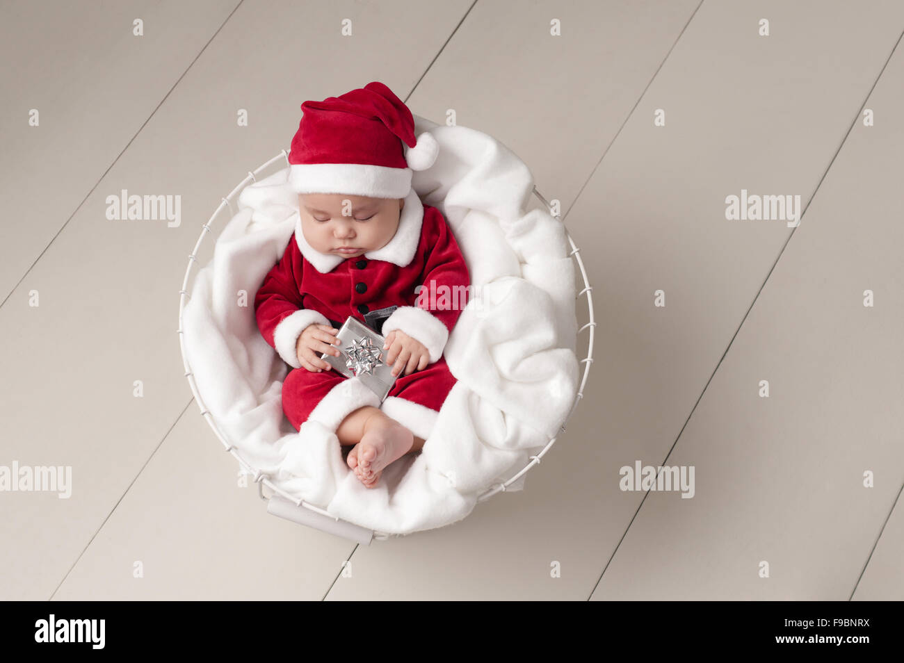 Tre mesi di età bambina indossa un Santa Claus costume, tenendo un piccolo dono e dormire in un cesto in filo. Foto Stock