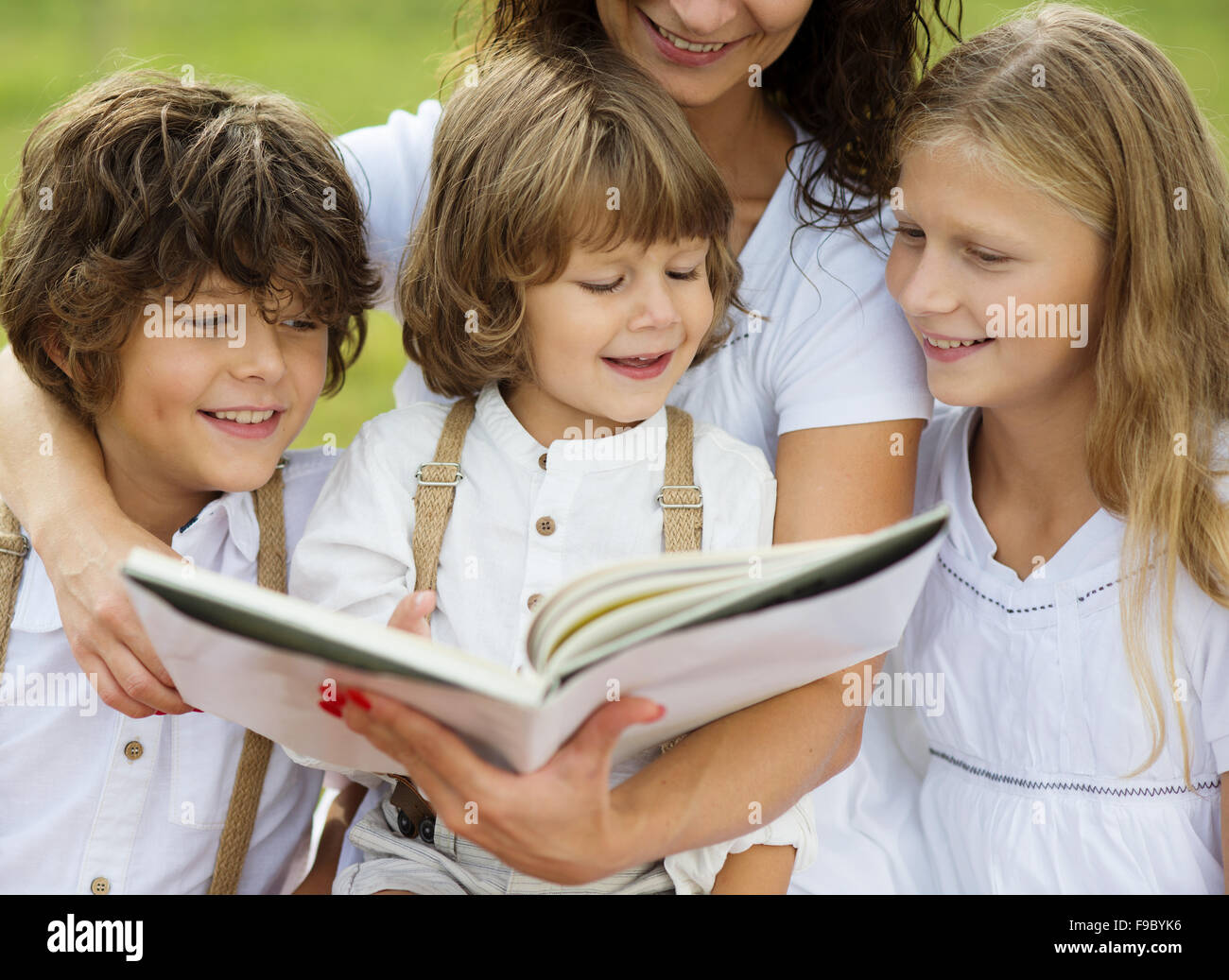 La madre è di posti a sedere e la lettura di un libro ai suoi figli nel parco verde Foto Stock