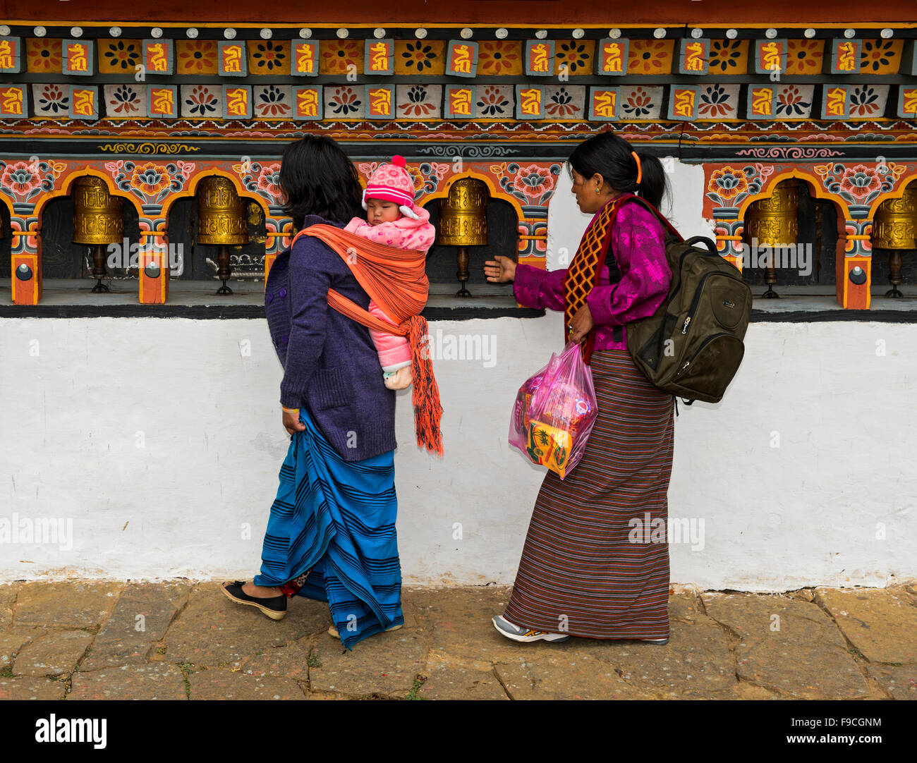 Due donne locali con un bimbo piccolo sul retro ruotando la preghiera Mills, monastero Chime Lhakhang vicino Lobesa, Bhutan Foto Stock