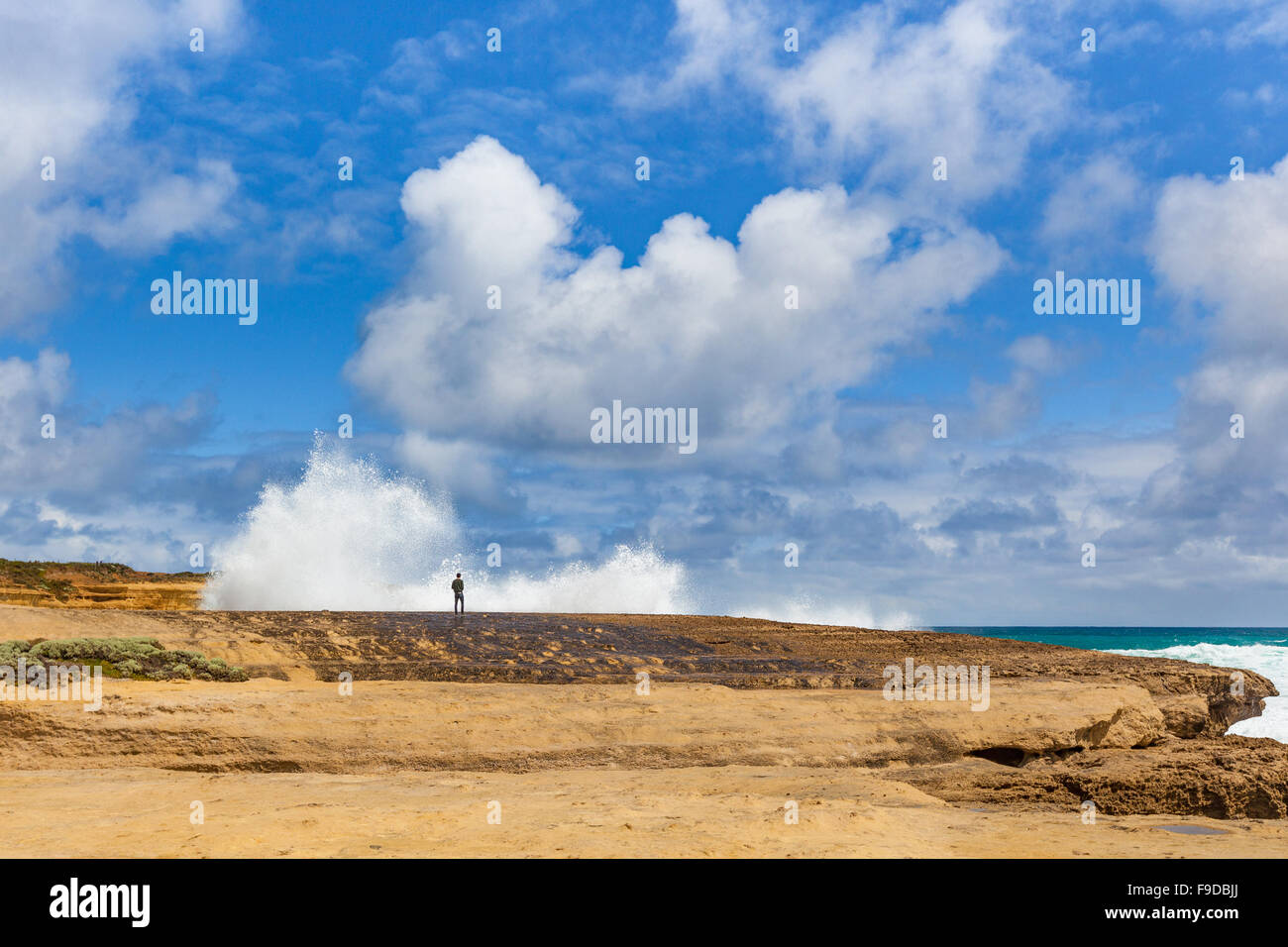 Una persona in piedi su una scogliera vicino gigantesca onda schizzi, Great Ocean Road, Australia Foto Stock