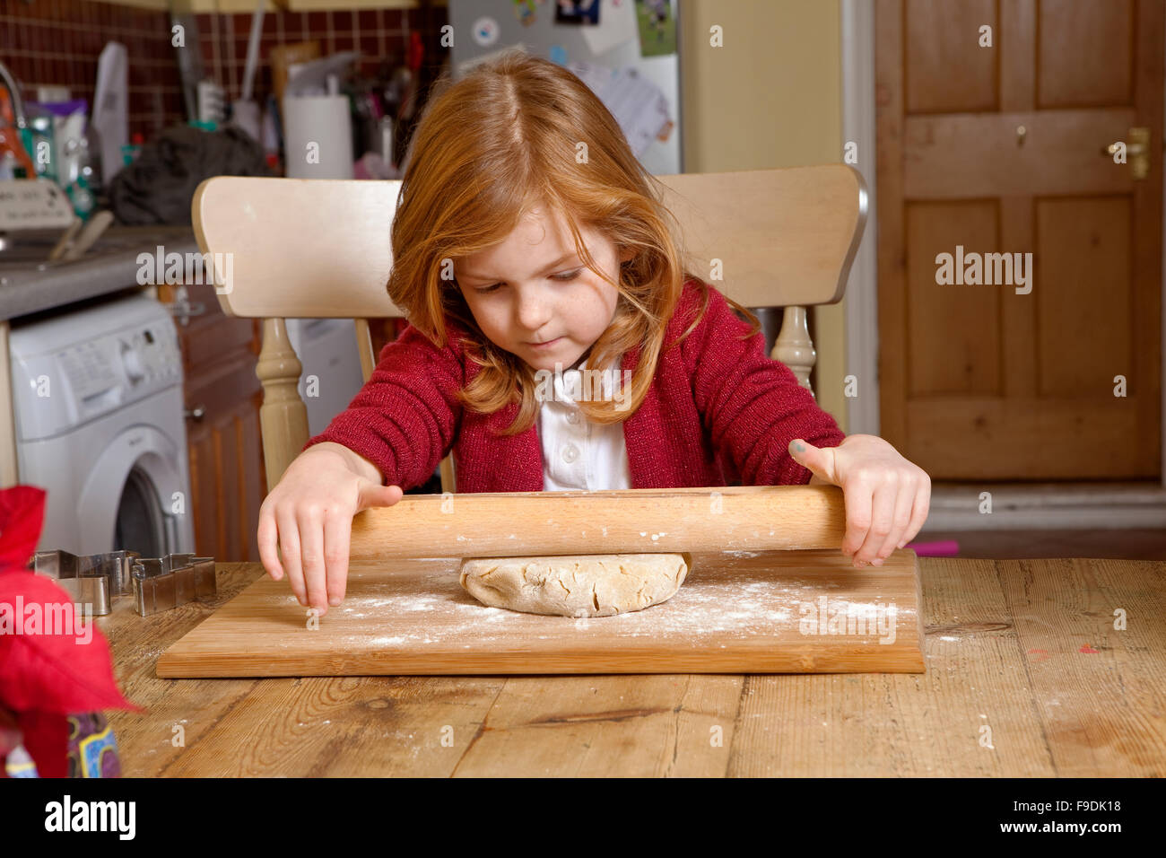 Una giovane ragazza è imparare i modi di cottura. Lei sta cercando di stendere la pasta per fare alcuni pan di zenzero biscotti. Foto Stock