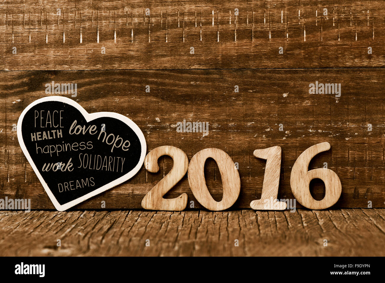Numeri in legno formando il numero 2016 e una a forma di cuore lavagna con alcuni auspici per il nuovo anno, come la pace, amore e Foto Stock