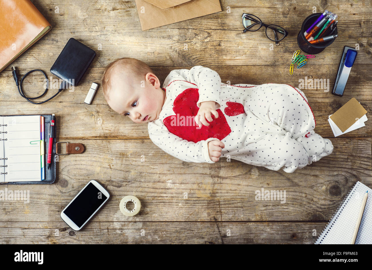 Mix di forniture per ufficio e gadget su una scrivania in legno a fianco di sfondo con carino piccolo bambino. Vista da sopra. Foto Stock