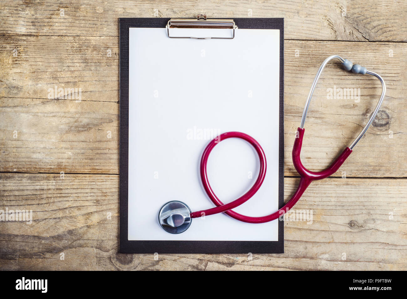 Luogo di lavoro di un medico. Lo stetoscopio e clip board sulla scrivania in legno sfondo. Foto Stock