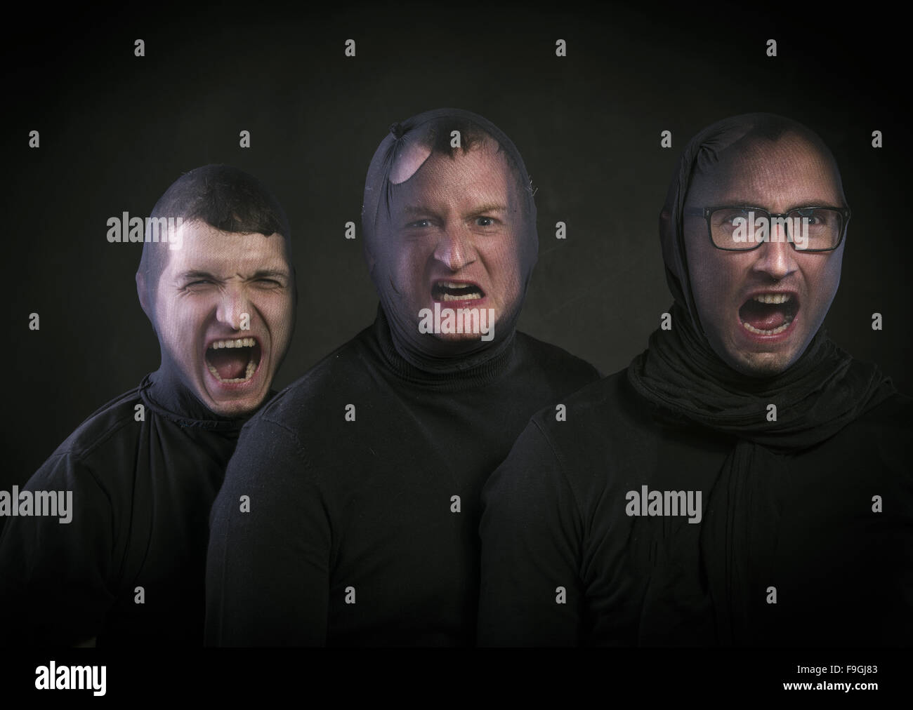 Tre ladri in passamontagna sui loro volti, vestito di nero. Studio shot su sfondo nero. Foto Stock