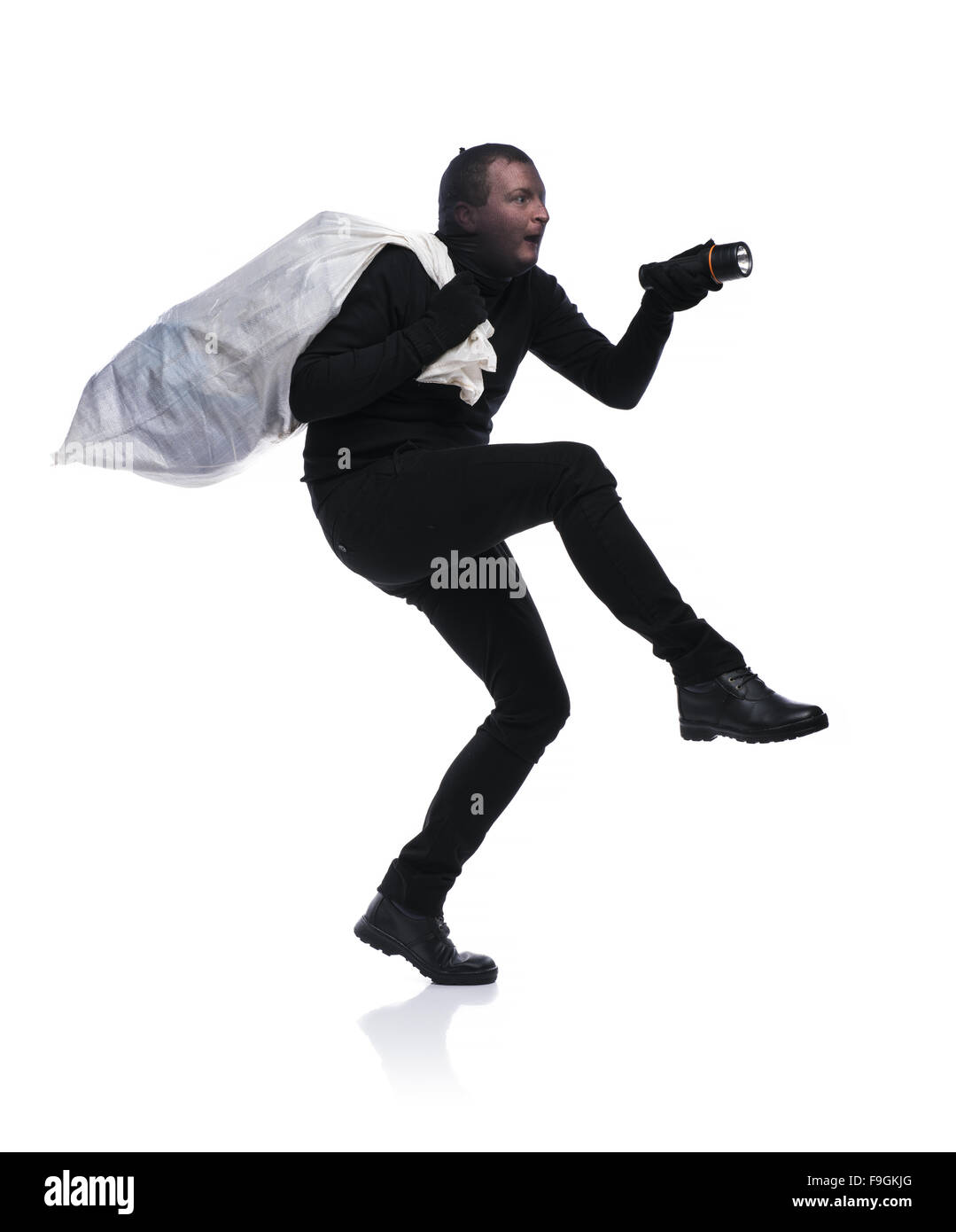 Ladro in azione con un grande sacco con passamontagna sul suo volto, vestito di nero. Studio shot su sfondo bianco. Foto Stock