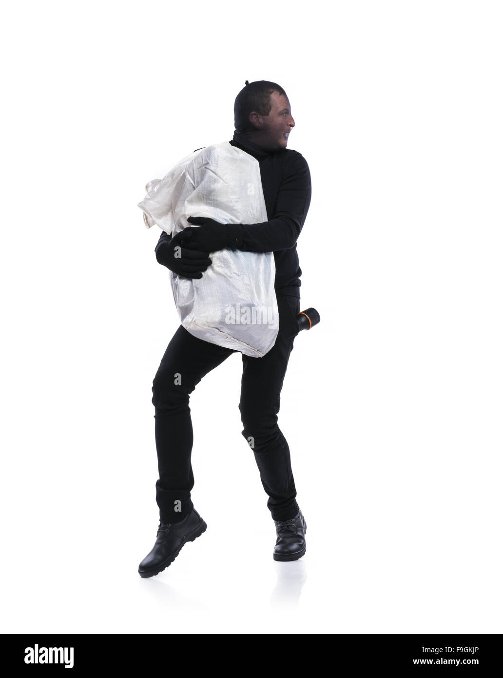 Ladro in azione con un grande sacco con passamontagna sul suo volto, vestito di nero. Studio shot su sfondo bianco. Foto Stock