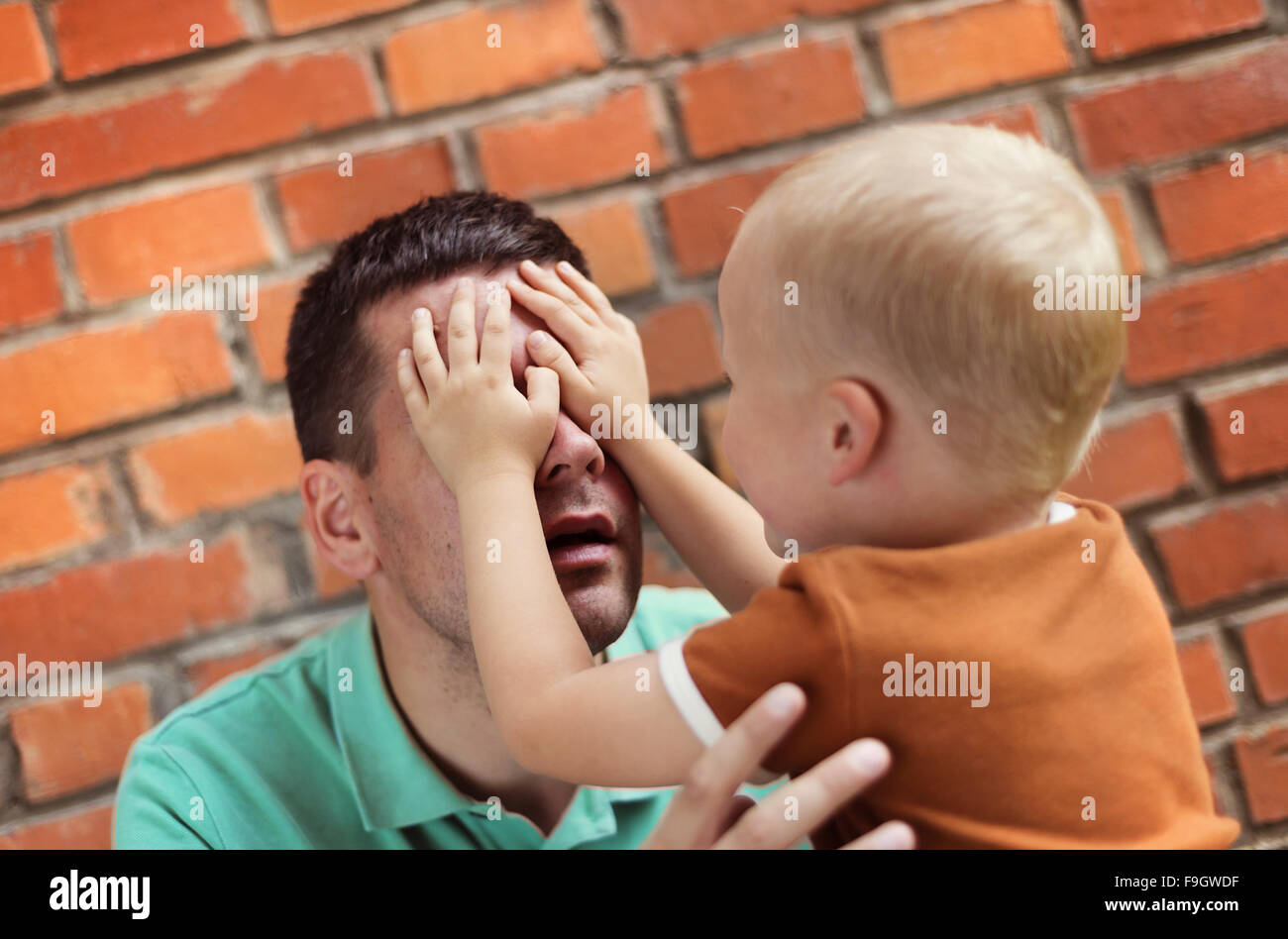Padre e figlio facendo facce buffe insieme su un muro di mattoni in background Foto Stock