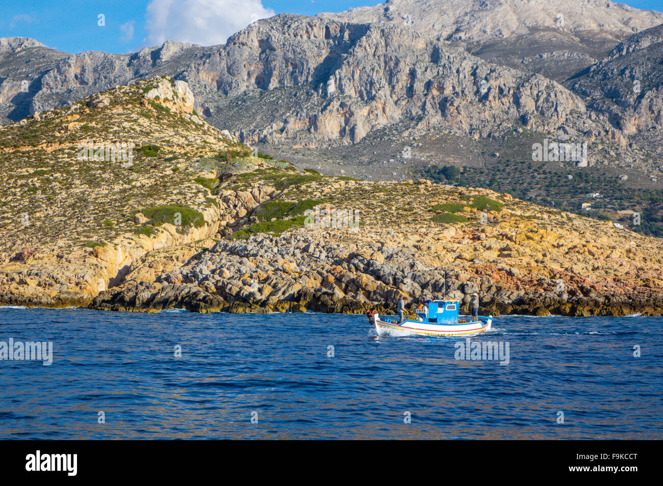 Di piccole dimensioni e di colore bianco e blu barca da pesca con due pescatori, mare azzurro e la costa rocciosa Foto Stock
