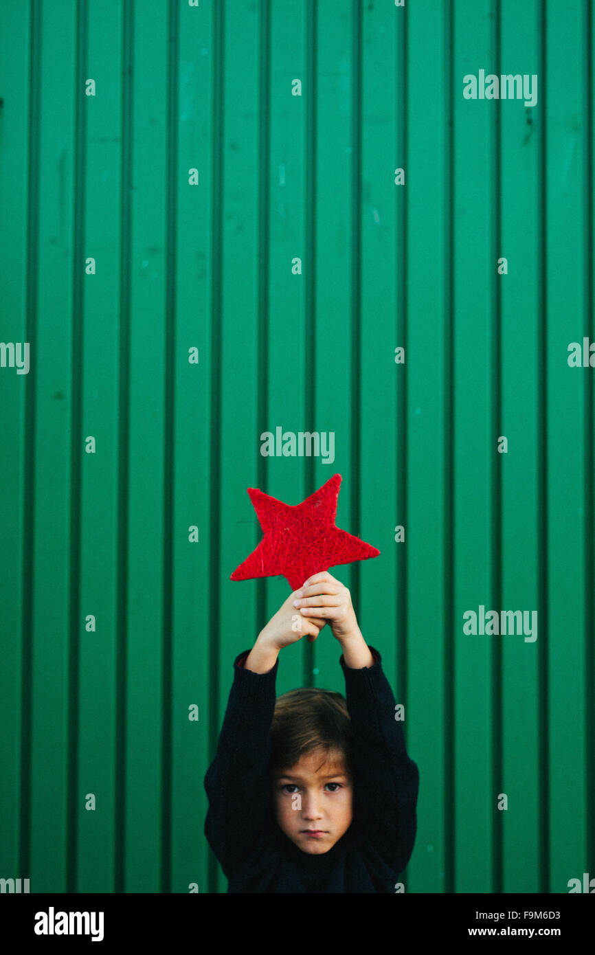 ragazzo di 6 anni che tiene una stella rossa su sfondo verde Foto Stock