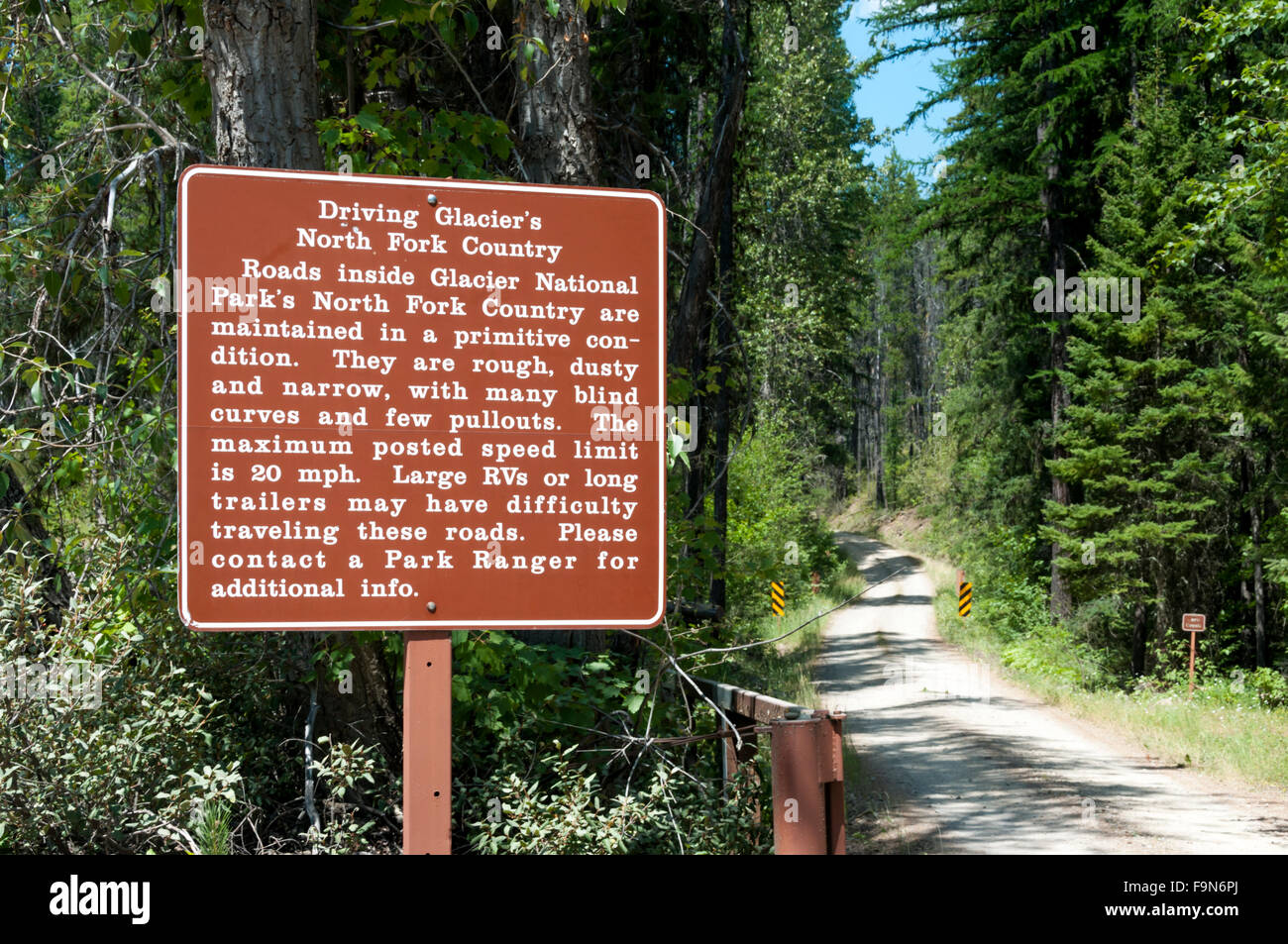 Un segnale di avvertimento circa la guida su backroads nella forcella del nord area del Glacier National Park, con una strada sterrata in background. Foto Stock