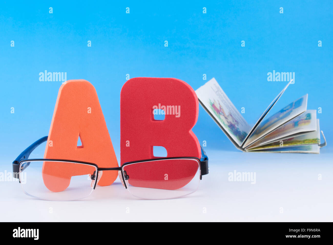 ABC lettere, occhiali e il libro aperto su sfondo blu Foto Stock