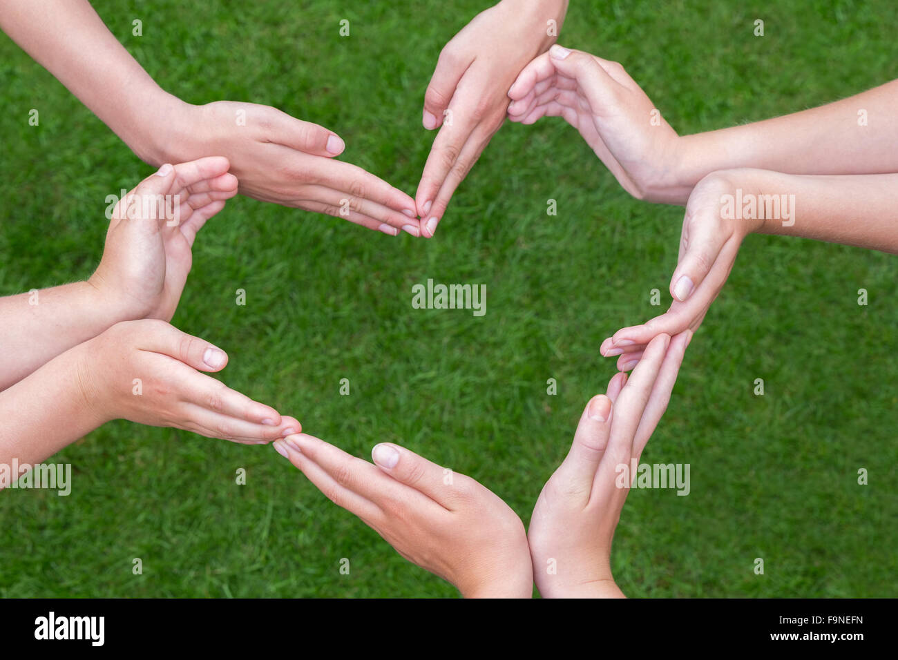Molte le braccia e le mani di ragazze fanno forma di cuore al di sopra di erba verde Foto Stock