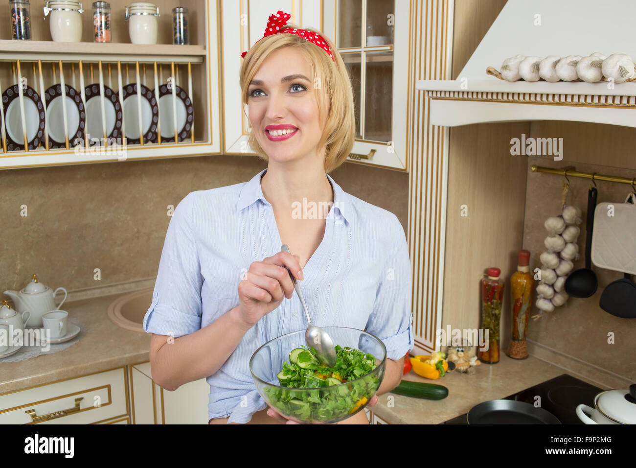 Ragazza cerca positivo e tenendo un recipiente con insalata. È in piedi in cucina Foto Stock