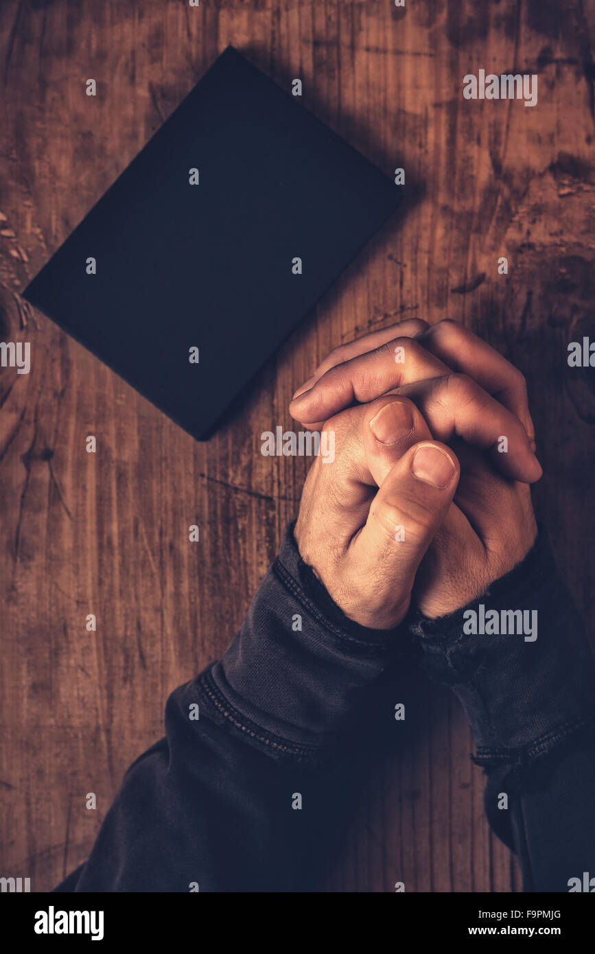 Mani piegate dell uomo cristiano pregare con la Bibbia al suo fianco sulla scrivania in legno nella chiesa, vista dall'alto Foto Stock