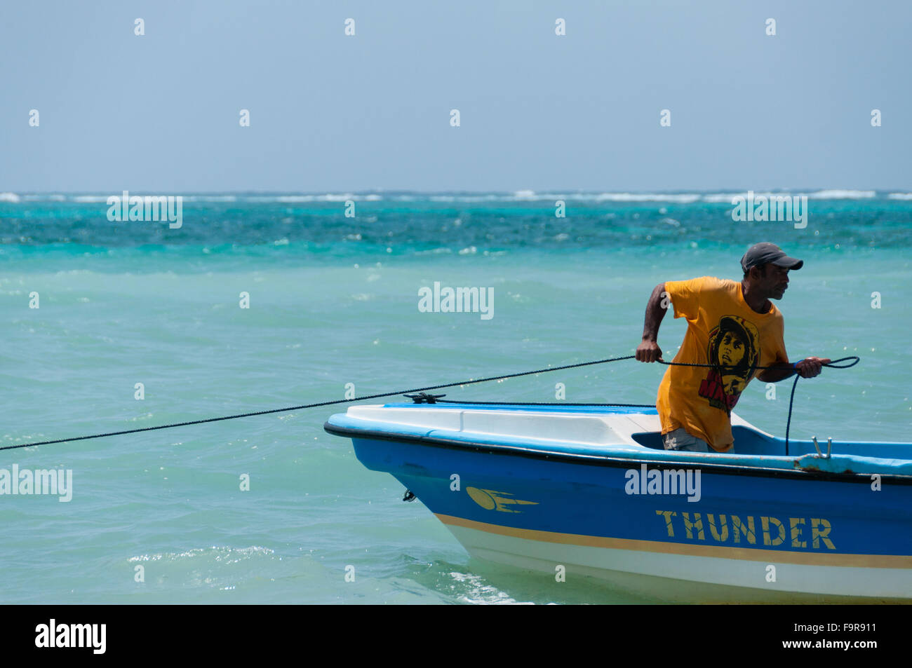 L'uomo con la maglietta gialla e hat sulla barca da pesca tirando una fune nell'oceano Foto Stock L'uomo con la maglietta gialla e hat sulla barca da pesca tirando una fune nell'oceano Foto Stock