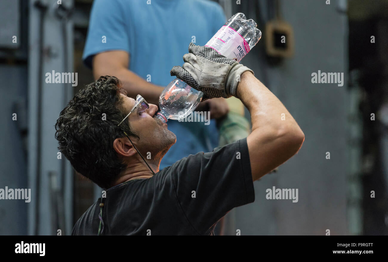 Esaurito dal calore del forno per vetro, una glassblower prende una pausa alla fabbricazione del vetro in Hergiswil, Svizzera. Foto Stock