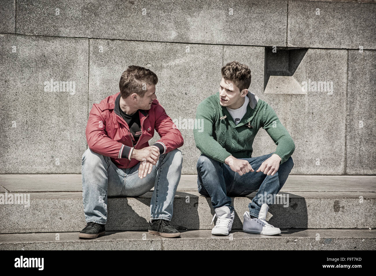 Due giovani uomini a parlare mentre è seduto sul cordolo. Estate Foto Stock