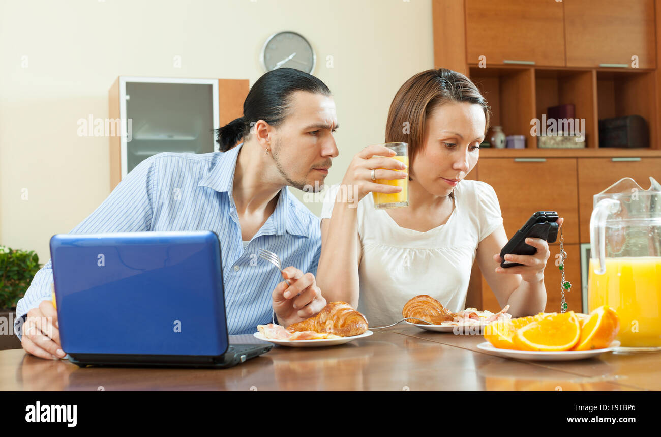 Paio utilizzando dispositivi durante il momento della colazione a casa Foto Stock