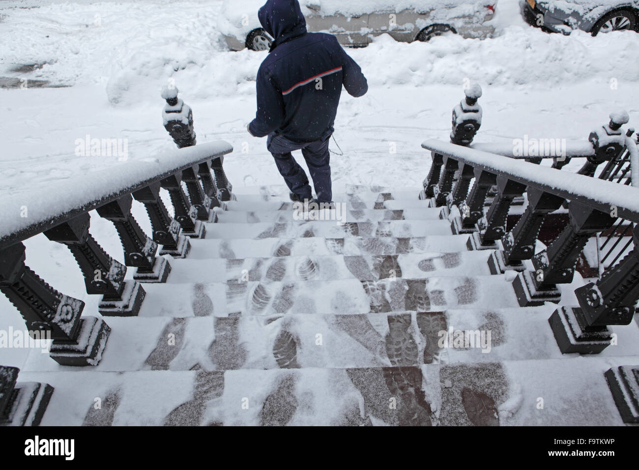 Consegna USPS uomo cammina verso il basso una coperta di neve arenaria townhouse stoop dopo la consegna di un pacchetto Foto Stock