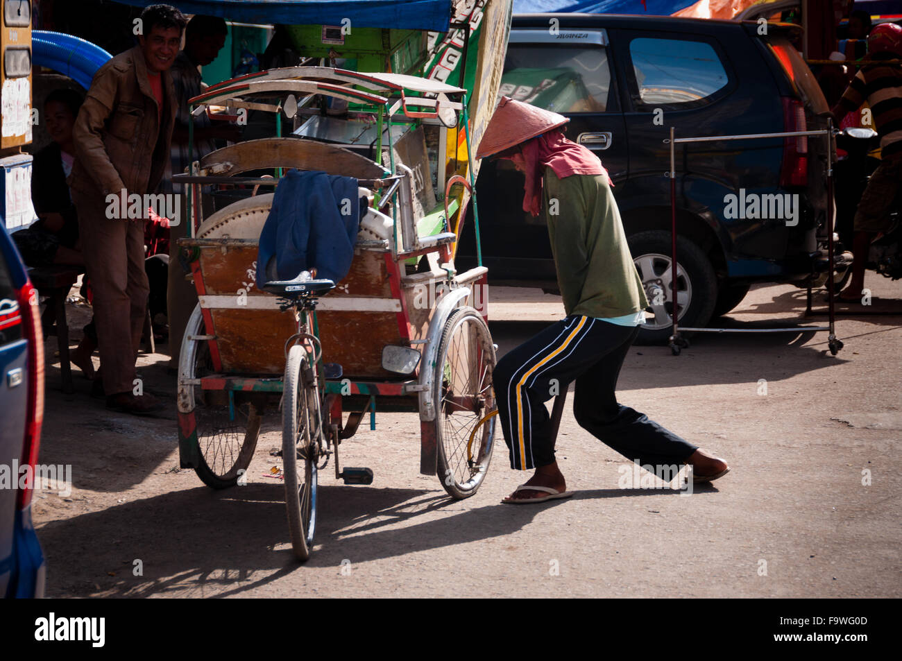 L'uomo con il cappello pompando aria nella ruota del suo triciclo Foto Stock