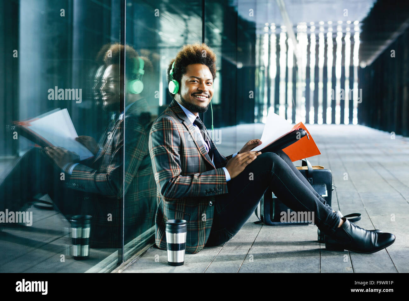Sorridente giovane imprenditore con le cuffie e la cartella seduti all'aperto Foto Stock