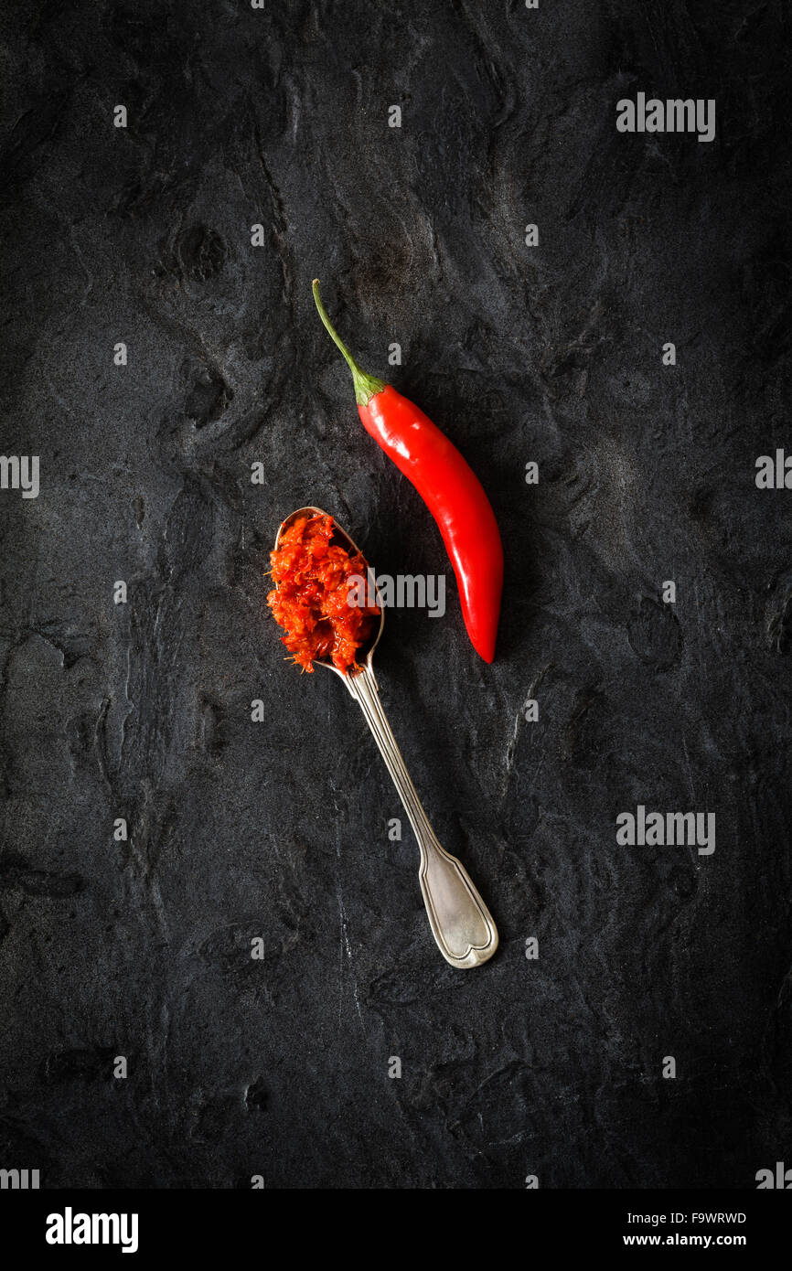 Cucchiaio di fatti in casa pasta di peperoncino e peperoncino pod sulla massa nero Foto Stock
