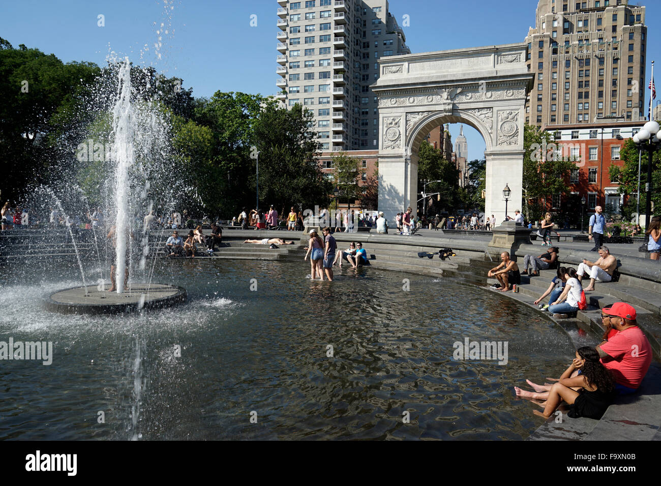 Visitatori relax presso la fontana centrale a Washington Square Park con Washington Square Arch in background, New York City Foto Stock