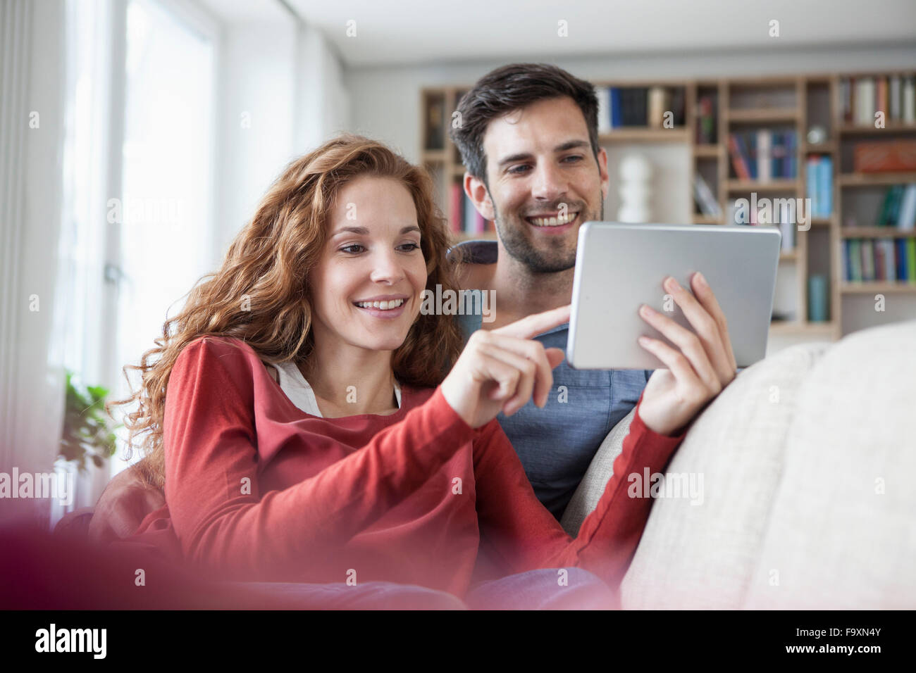 Rilassata giovane a casa sul lettino usando tavoletta digitale Foto Stock
