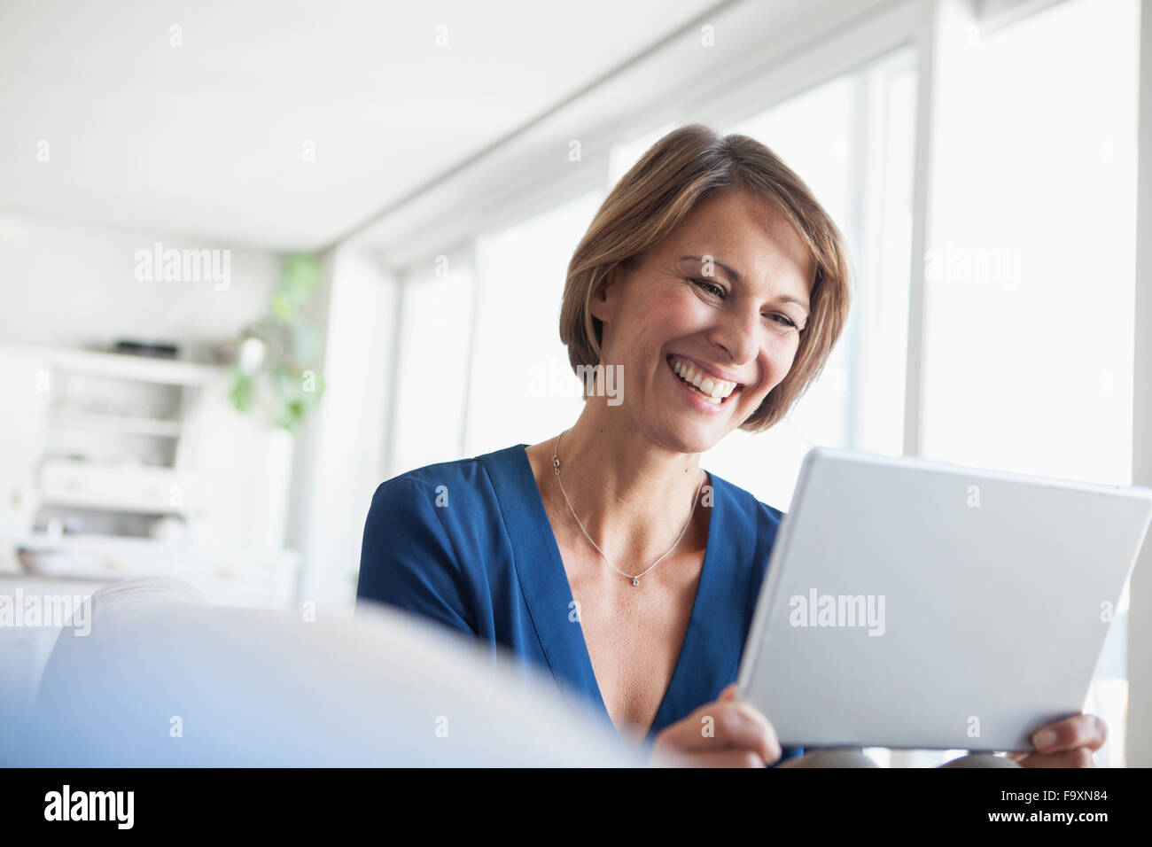Donna sorridente a casa utilizzando la tavoletta digitale Foto Stock