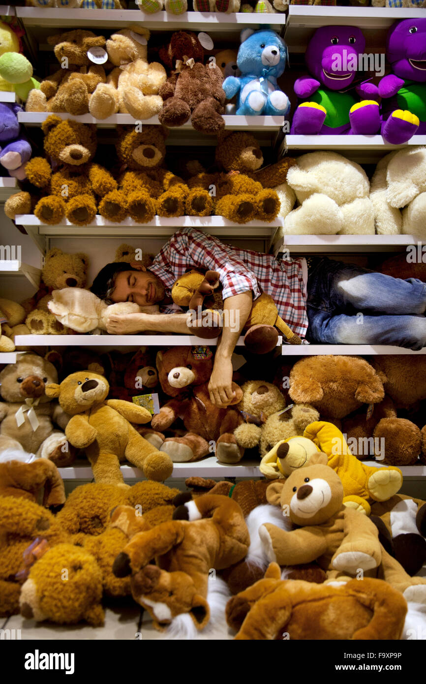 Uomo di dormire su un ripiano tra giocattoli morbidi in un supermercato Foto Stock