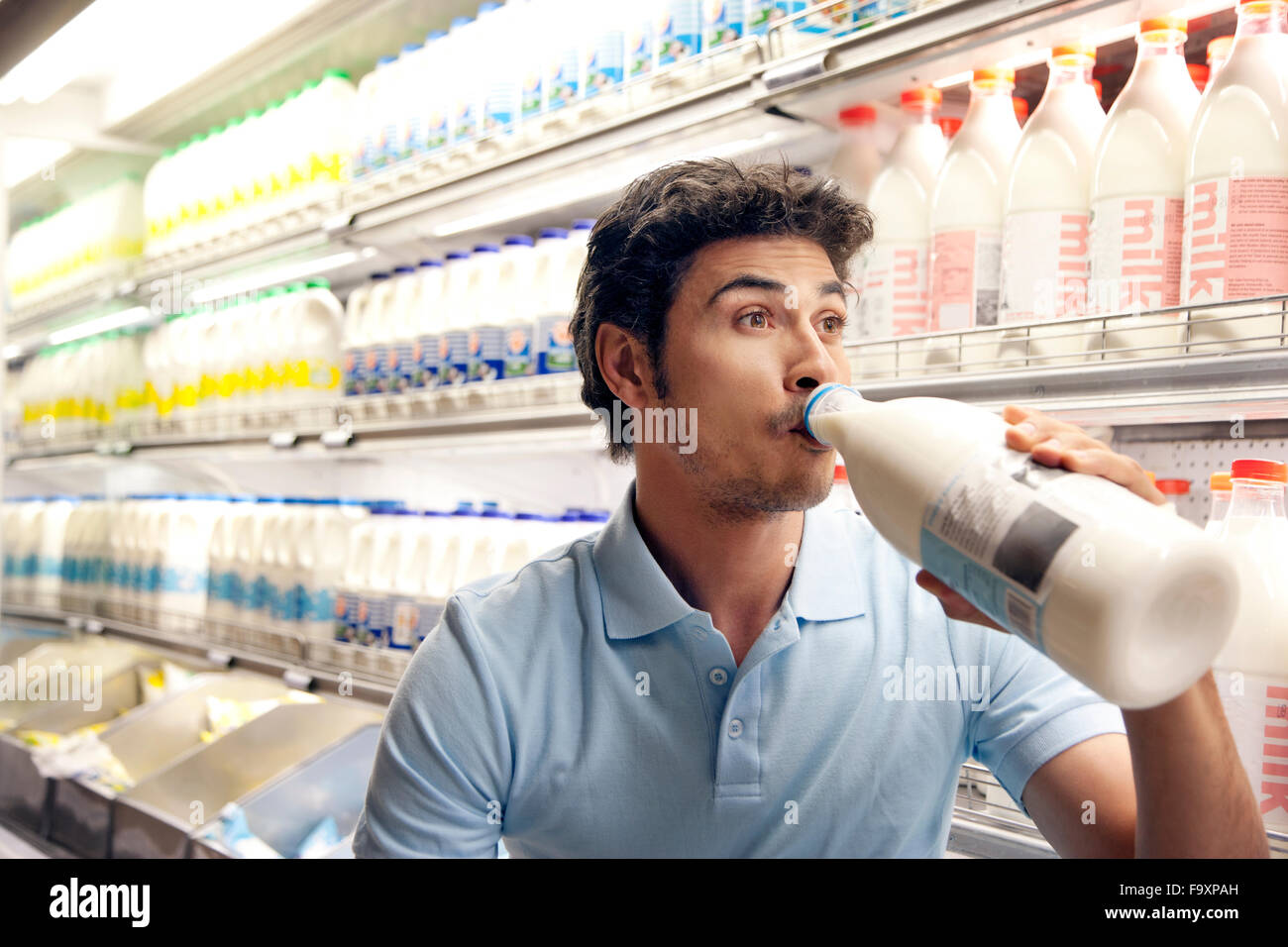 Uomo di bere latte nella parte anteriore del frigorifero in un supermercato Foto Stock