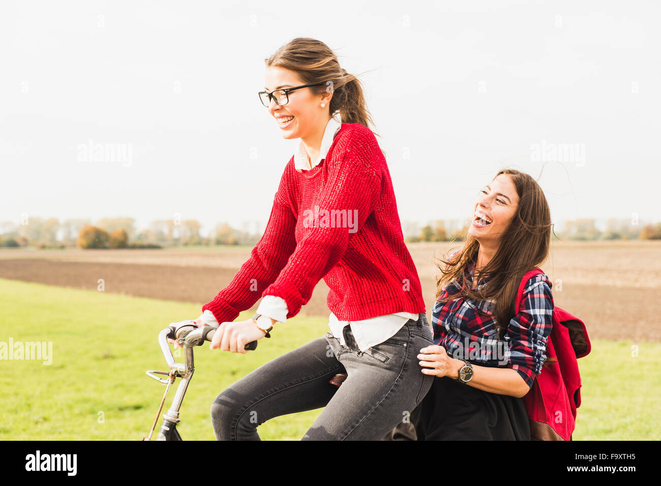 Felice di due giovani donne che condividono una bicicletta nel paesaggio rurale Foto Stock