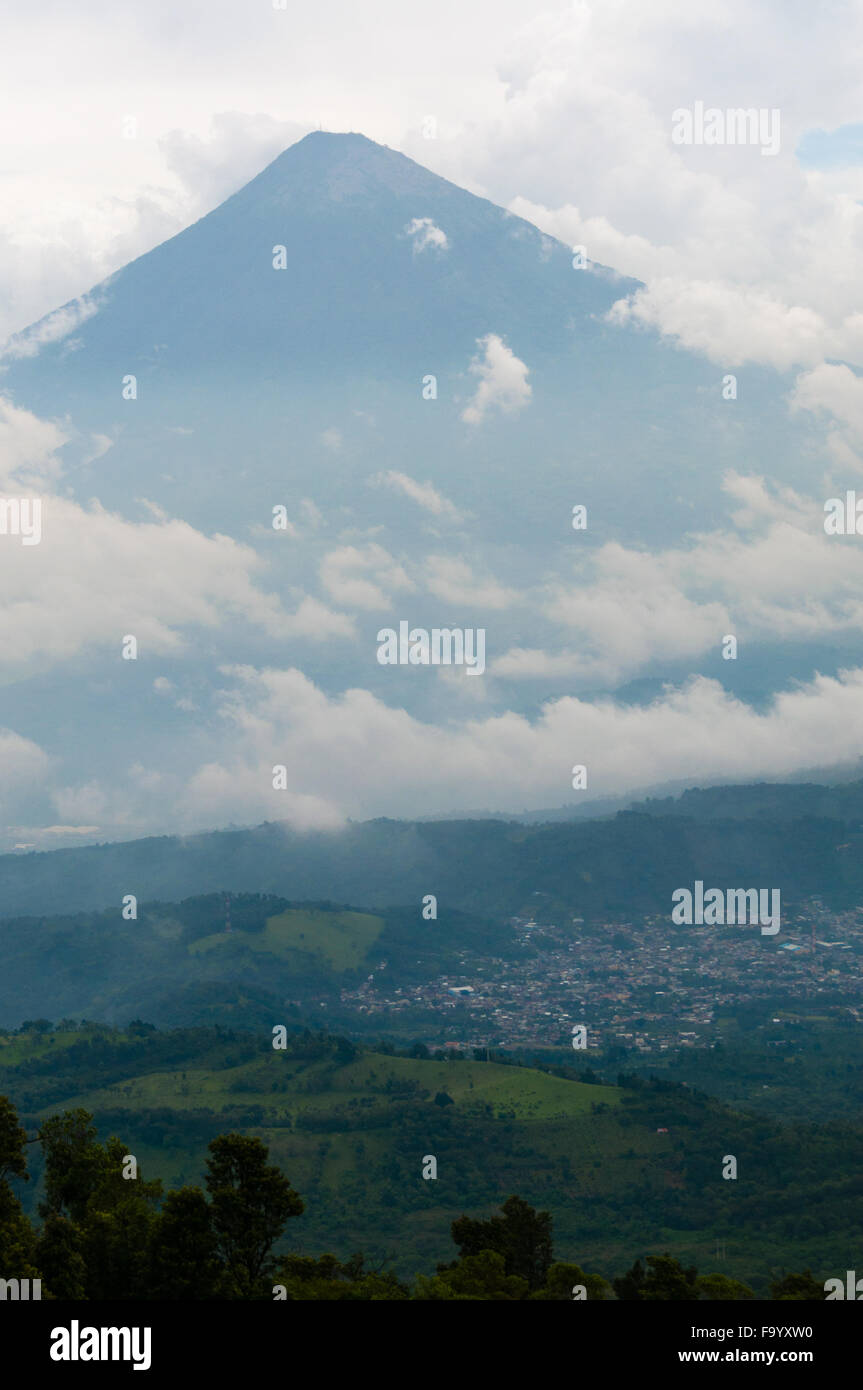 Grande cima del vulcano circondato dalla nebbia e nuvole sopra il campo verde Foto Stock