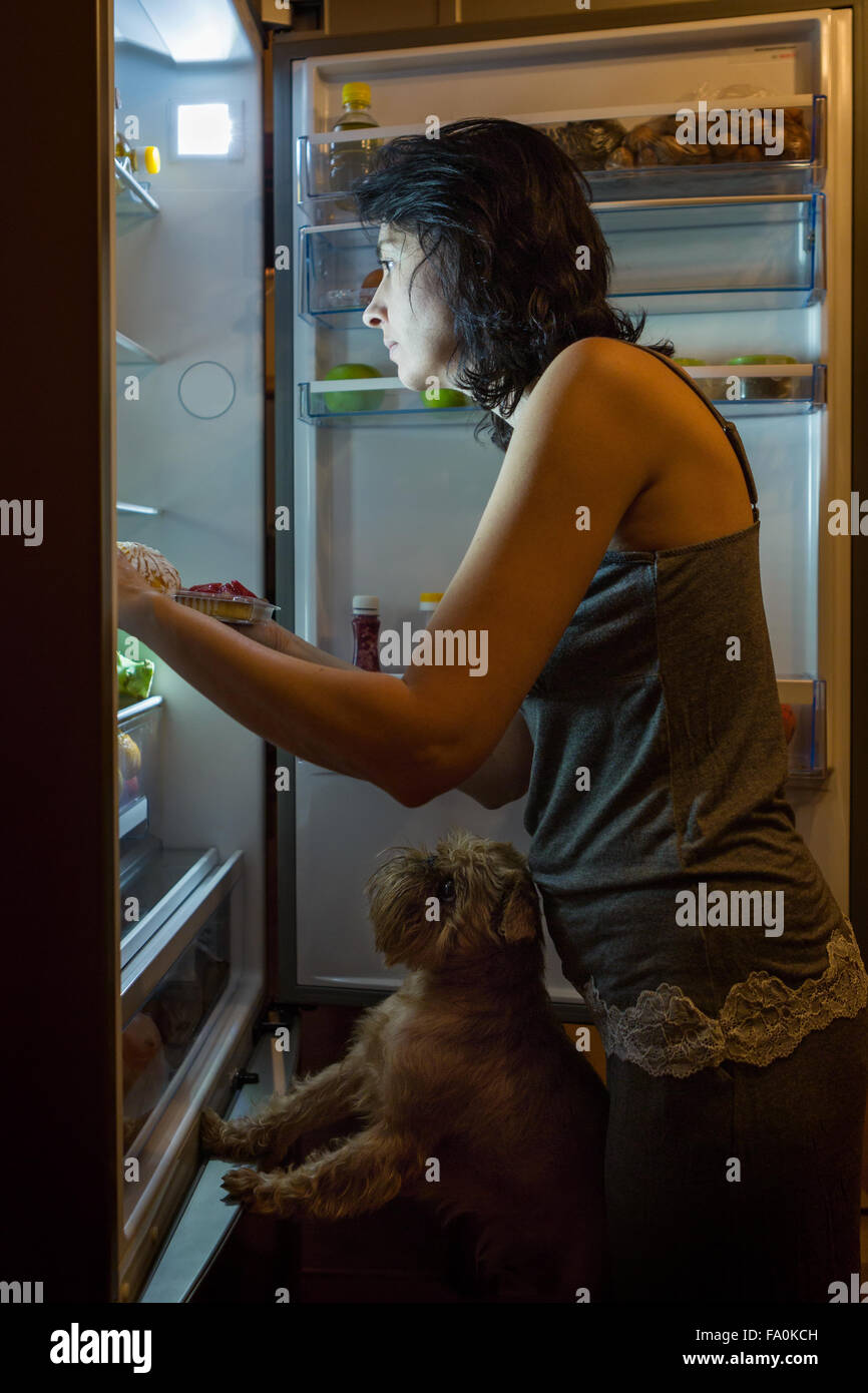 La donna e il cane di notte in cerca di cibo nel frigo Foto Stock