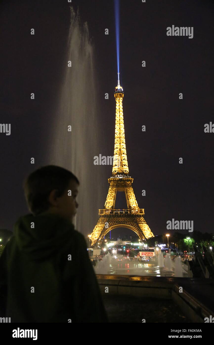 La torre Eiffel di notte con la luce di ricerca sulla punta della torre skyward trainato in background di un bambino silhouette Foto Stock